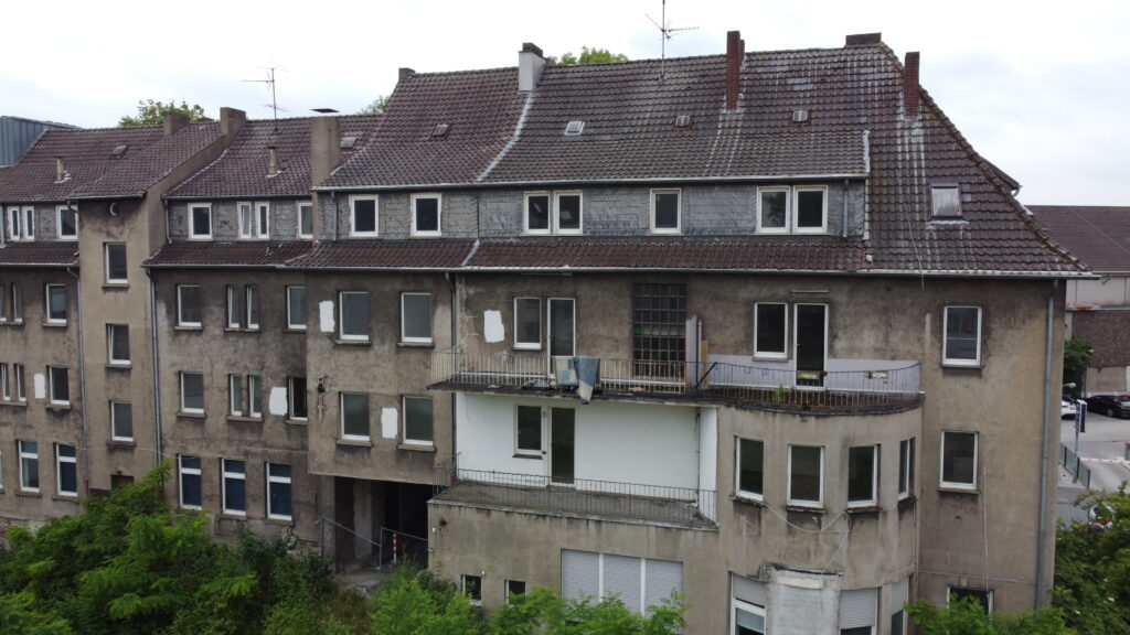 Altbau-Mehrfamilienhaus mit verwittertem Ziegeldach vor der Sanierung, Luftaufnahme der Innenhof-Fassade.