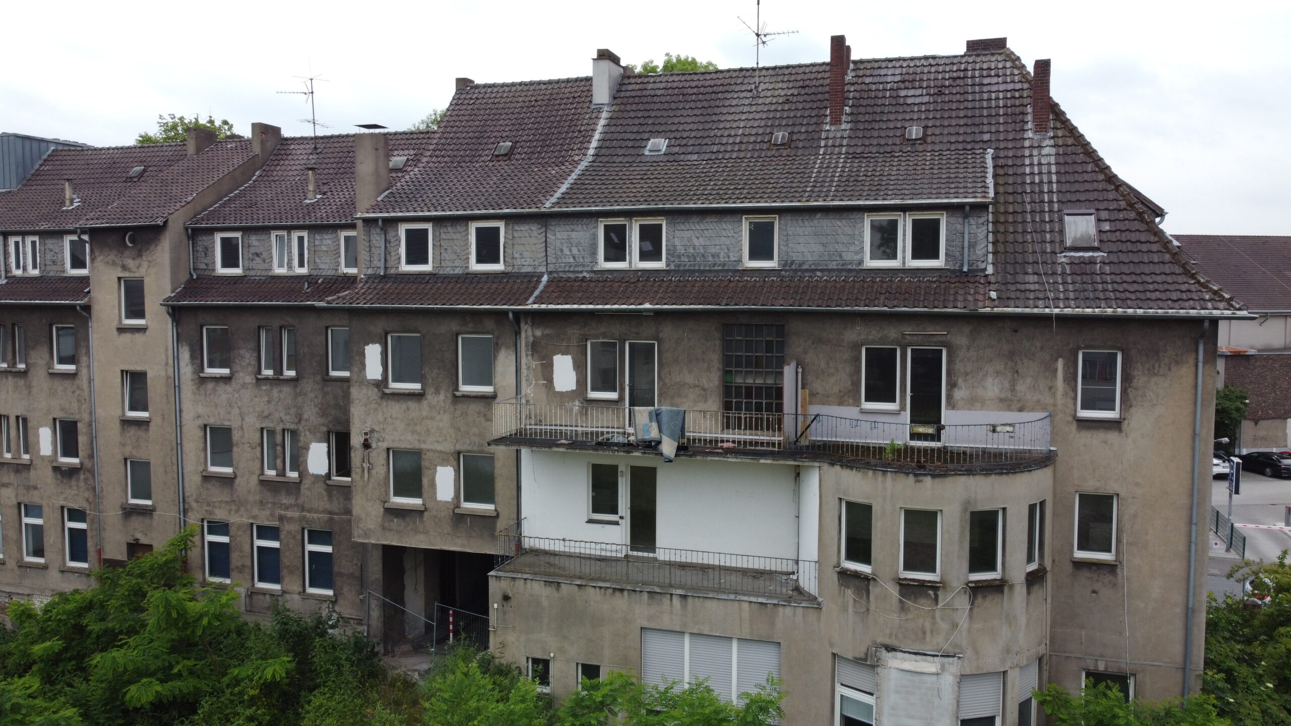 Altbau-Mehrfamilienhaus mit verwittertem Ziegeldach vor der Sanierung, Luftaufnahme der Innenhof-Fassade.