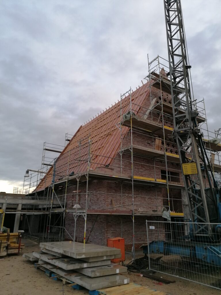 Rohbau der Kirche mit sichtbarer Dachlattung vor der Eindeckung, eingerüstet, Baukran im Hintergrund.