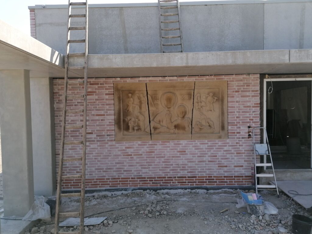 Klinkerfassade der Kirche im Rohbau mit Steinrelief 'Ite ad Joseph' zwischen zwei Leitern.