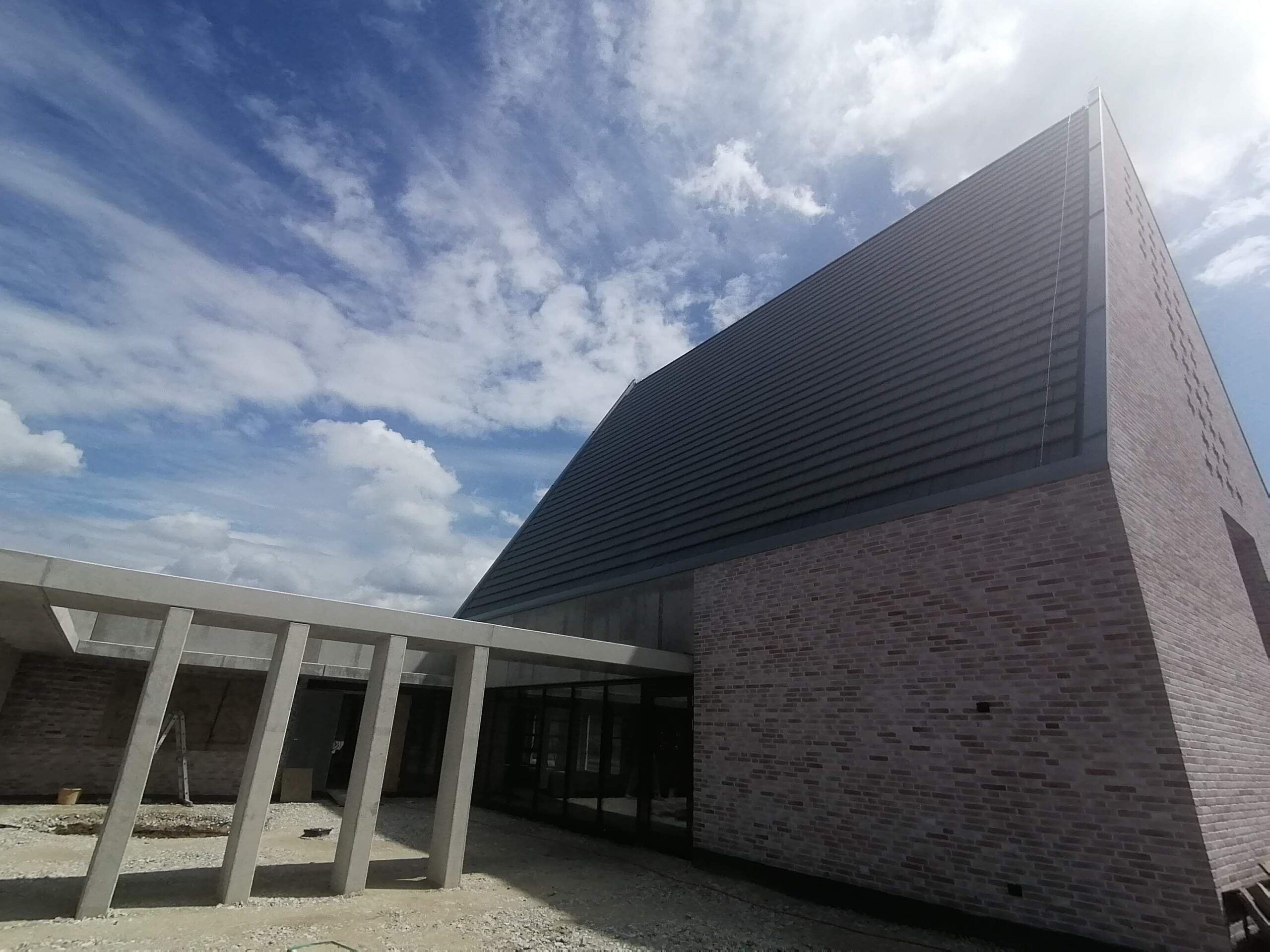Modernes Kirchengebäude mit spitz zulaufendem anthrazitfarbenem Metall-Stehfalzdach und Klinkerfassade, Ansicht von schräg unten.