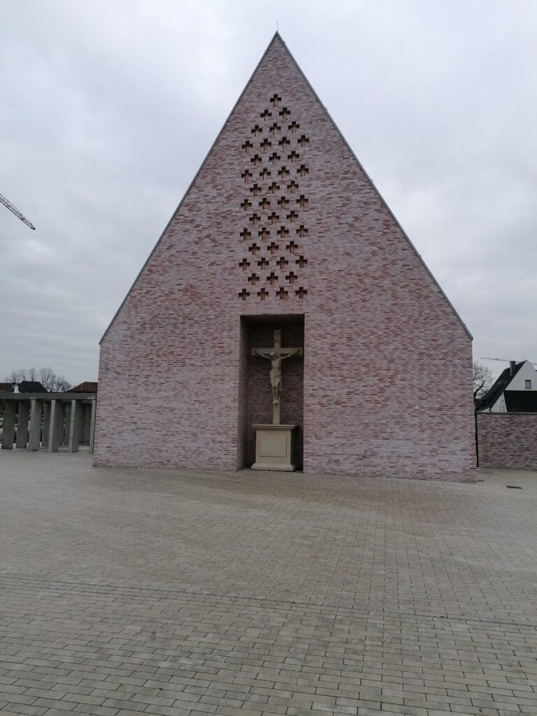 Giebelfassade der Kirche mit kreuzförmigem Lochmuster aus Klinkersteinen und Kruzifix am Eingang.